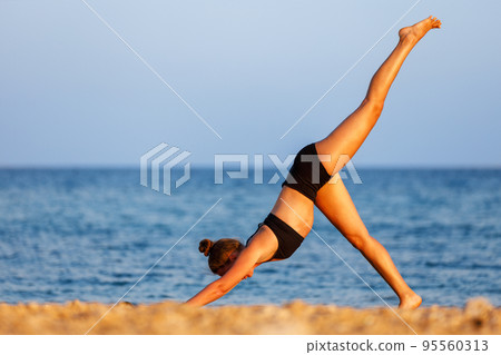 Young woman doing three legged dog pose on her yoga routine at the beach 95560313