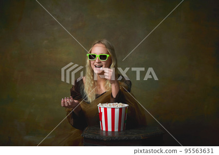 Cheerful young girl in image of Mona Lisa in 3d eyewear wathich movie over dark vintage background. Retro style, art, fashion, comparison of eras concept. Cheerful young girl in image of Mona Lisa in 3d eyewear wathich movie over dark vintage background. Retro style, art, fashion, comparison of eras concept. 95563631