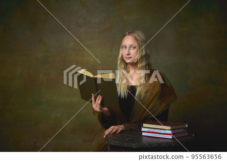 Beautiful young girl with long blonde hair wearing medieval dress reading book over dark vintage background. Retro style, art, fashion, comparison of eras concept. Beautiful young girl with long blonde hair wearing medieval dress reading book over dark vintage background. Retro style, art, fashion, comparison of eras concept. 95563656