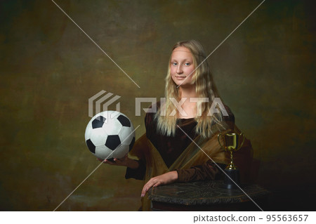 Football fan. Vintage style portrait of young charming girl in image of Mona Lisa, La Gioconda holding football ball isolated on dark background. Sport, betting, art Football fan. Vintage style portrait of young charming girl in image of Mona Lisa, La Gioconda holding football ball isolated on dark background. Sport, betting, art 95563657
