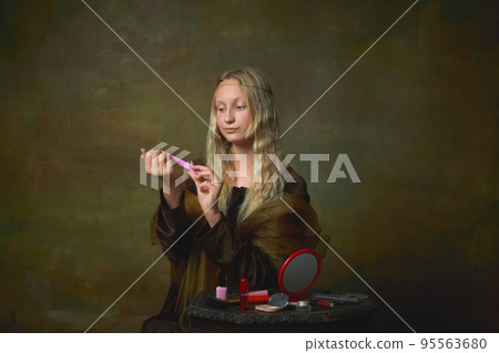 Elegant young girl with long blonde hair wearing medieval dress like Mona Lisa replica over dark vintage background. Vintage style, art, fashion, comparison of eras concept. Elegant young girl with long blonde hair wearing medieval dress like Mona Lisa replica over dark vintage background. Vintage style, art, fashion, comparison of eras concept. 95563680