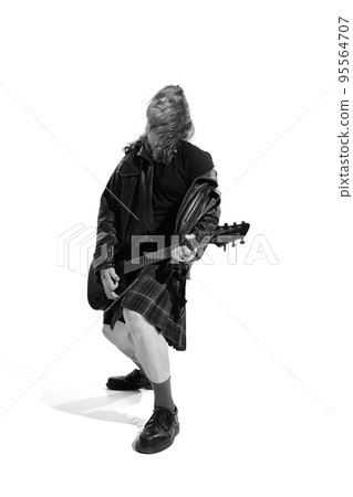 Portrait of expressive young man with long hair, rock musician playing guitar over white background. Black and white photography Portrait of expressive young man with long hair, rock musician playing guitar over white background. Black and white photography 95564707