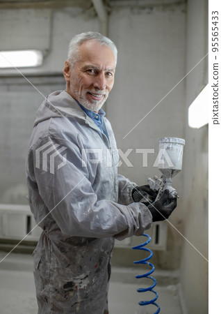 Man with a spray gun standing in a painting room 95565433