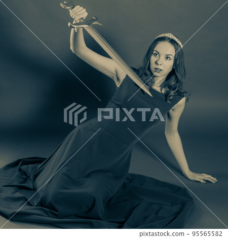 An attractive girl who fell to her knees defending herself with a sword. Halloween sepia toned 95565582