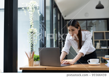 Concentrated young business woman working on her computer. Start-up office background 95566439