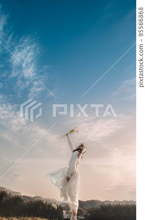 一個穿著白色連衣裙的女人在藍天下捧著鮮花 95566868