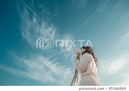 A woman in a white dress holding flowers under the blue sky A woman in a white dress holding flowers under the blue sky 95566869
