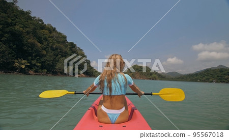 Sportive woman rows pink plastic canoe along sea water. 95567018