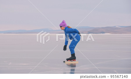The child train on ice professional speed skating. The girl skates in the winter in sportswear, sport glasses, suit. Outdoor slow motion. 95567140