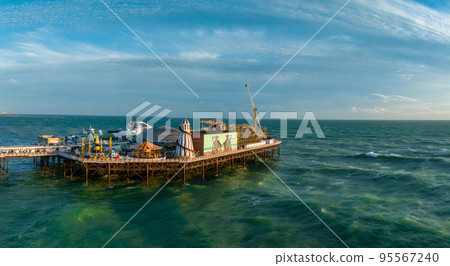 Aerial view of Brighton Palace Pier, with the seafront behind. Aerial shot of the stunning city of Brighton and Hove with seagulls flying around at sunset. 95567240