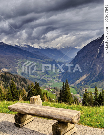Wooden bench made of rough logs for tired hikers in front of long wide valley between majestic mountains of high alps in Austria Wooden bench made of rough logs for tired hikers in front of long wide valley between majestic mountains of high alps in Austria 95567643
