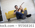Lifestyle portrait of attractive handsome man with pleasant smile relaxing and sitting play guitar at living room 95568161