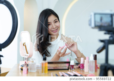 online trading business, a beautiful young woman working independently at home reviewing cosmetic products through the camera to customers to increase their interest in making a purchase decision. 95569722