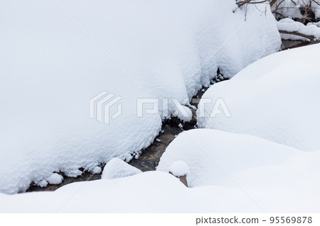 A stream flowing between a large layer of snow in winter A stream flowing between a large layer of snow in winter 95569878