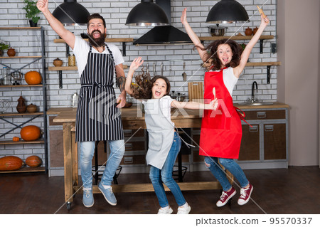 Home party. Happy family jump. Father, mother and child chef cooking. Little girl with parents in apron. Mother and father with little girl. Family day. Happy family in kitchen. Happy family morning Home party. Happy family jump. Father, mother and child chef cooking. Little girl with parents in apron. Mother and father with little girl. Family day. Happy family in kitchen. Happy family morning 95570337
