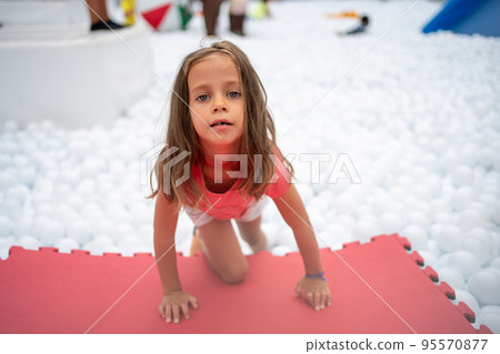 Happy little girl playing white plastic balls pool in amusement park. Happy little girl playing white plastic balls pool in amusement park. 95570877