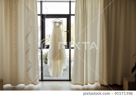 A beautiful and delicate dress hangs by the window A beautiful and delicate dress hangs by the window 95571396
