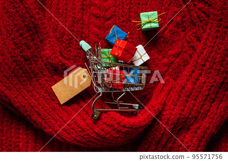 Christmas xmas shopping banner with mockup label. Shopping cart with many gift boxes with cardboard label on red knitting background 95571756