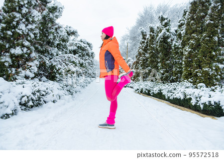 Winter workout, Winter fitness, exercising in cold weather. Sportswoman doing stretching exercises and preparing to run in nature at snowy winter park. 95572518