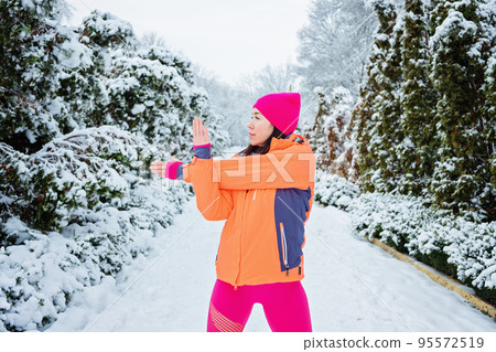 Winter workout, Winter fitness, exercising in cold weather. Sportswoman doing stretching exercises and preparing to run in nature at snowy winter park. Winter workout, Winter fitness, exercising in cold weather. Sportswoman doing stretching exercises and preparing to run in nature at snowy winter park. 95572519