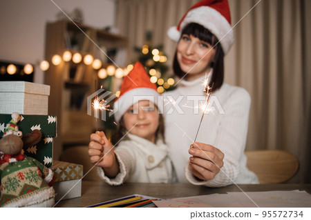 Focus on hands with sparkles, blur background of cheerful girl and her mother with charming smile 95572734