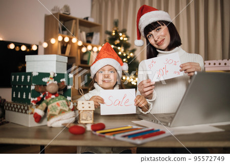 Young lovely mother and cute charming daughter kid in red hats holding letter with sale inscription 95572749