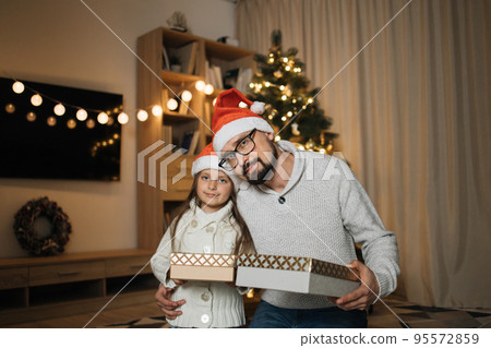 Young happy father and little cute daughter in santa hats sitting with gifts after decorating tree Young happy father and little cute daughter in santa hats sitting with gifts after decorating tree 95572859