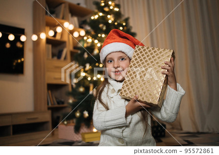 Little adorable girl in knitted sweater with present near her ear trying to guess what is inside box Little adorable girl in knitted sweater with present near her ear trying to guess what is inside box 95572861