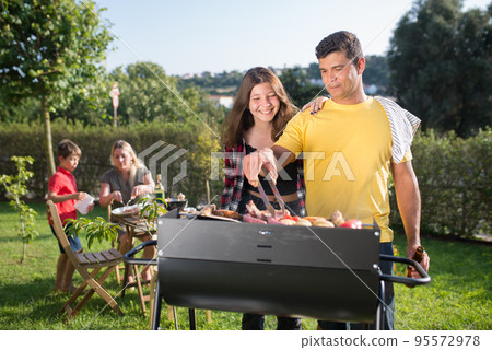 Content father grilling meat and vegetables with daughter Content father grilling meat and vegetables with daughter 95572978