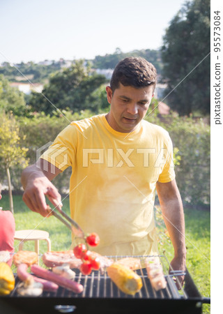 Pleased mid adult man grilling steak and corn 95573084