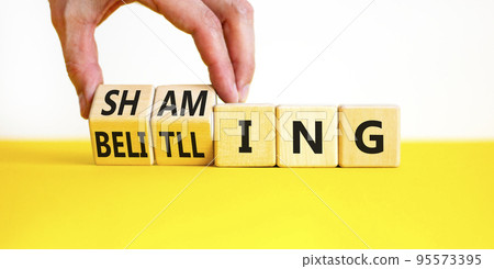 Shaming and belittling symbol. Concept words Shaming and Belittling on wooden cubes. Businessman hand. Beautiful yellow table white background. Business shaming and belittling concept. Copy space. Shaming and belittling symbol. Concept words Shaming and Belittling on wooden cubes. Businessman hand. Beautiful yellow table white background. Business shaming and belittling concept. Copy space. 95573395