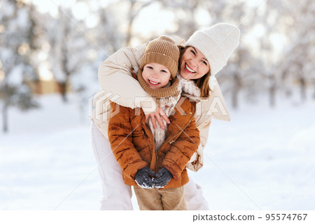 Happy mother embracing little boy son while having fun in snowy weather outdoor 95574767