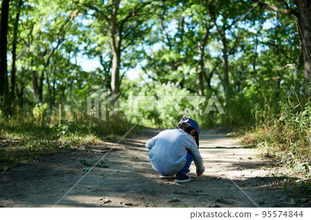 一個男孩蹲在森林裡的一條人行道上，擔心土壤 95574844