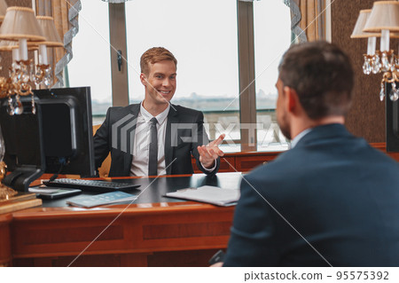 Smiling hotel receptionist helping Businessman to check in and receive key from room Smiling hotel receptionist helping Businessman to check in and receive key from room 95575392