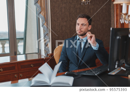 Focused businessman in suit sitting in luxury hotel room and using computer Focused businessman in suit sitting in luxury hotel room and using computer 95575393