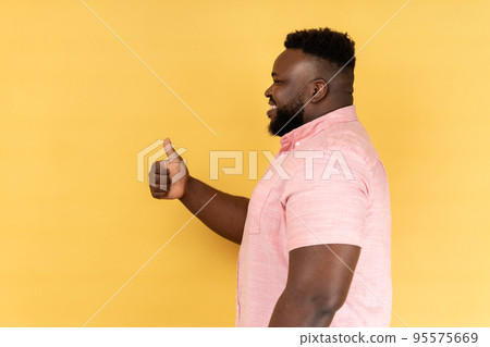 Side view of pleased optimistic smiling man wearing pink shirt showing thumbs up gesture, doing success sign with hand, approved excellent job. Indoor studio shot isolated on yellow background. 95575669