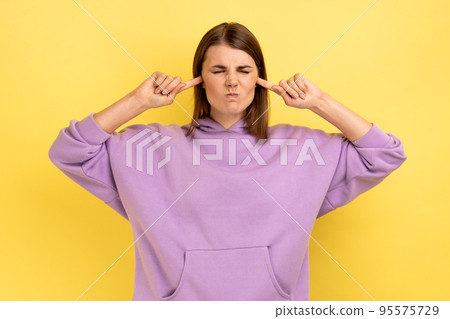 Don't want to listen. Beautiful irritated stressed out woman clothing covering ears, keeping eyes closed, nervous breakdown, wearing purple hoodie. Indoor studio shot isolated on yellow background. Don't want to listen. Beautiful irritated stressed out woman clothing covering ears, keeping eyes closed, nervous breakdown, wearing purple hoodie. Indoor studio shot isolated on yellow background. 95575729