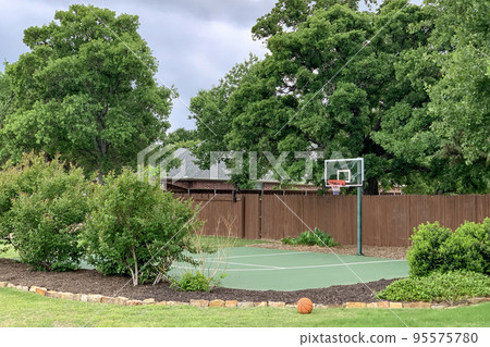 Outdoor shot of backyard of country house in the suburbs with trees, bushes, flowerbed and basketball court, zone for activity at home. 95575780