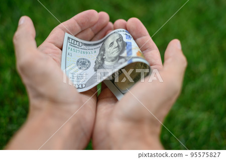 Close up 100 Dollar bank note in hand on grass background. One hundred American dollars. Close up 100 Dollar bank note in hand on grass background. One hundred American dollars. 95575827
