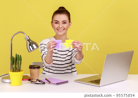 Happy smiling woman putting together two colored pieces of jigsaw, easily solving difficult tasks at work, sitting at workplace with laptop. Indoor studio studio shot isolated on yellow background. Happy smiling woman putting together two colored pieces of jigsaw, easily solving difficult tasks at work, sitting at workplace with laptop. Indoor studio studio shot isolated on yellow background. 95575854