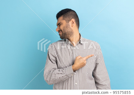 Get out. Portrait of serious angry businessman pointing finger, sneak male blaming another people, turning face, wearing striped shirt. Indoor studio shot isolated on blue background. Get out. Portrait of serious angry businessman pointing finger, sneak male blaming another people, turning face, wearing striped shirt. Indoor studio shot isolated on blue background. 95575855