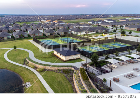 Aerial view of large tennis courts, swimming pool at community recreational center with mansions with lounge zones in the summertime outdoor. 95575872