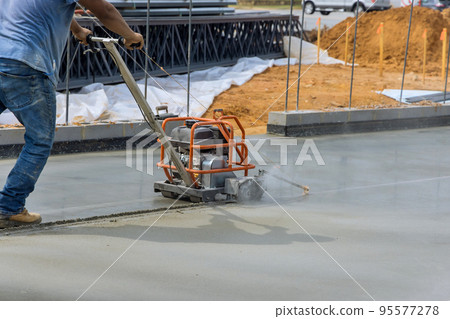Worker using cutting machine are cutting concrete for expansion isolation joint of foundation concrete after pouring in construction site 95577278