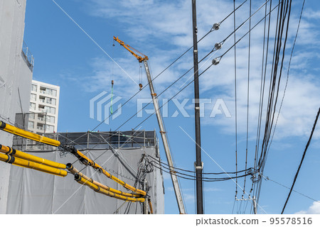 Crane and electric wire protection pipe at a construction site Crane and electric wire protection pipe at a construction site 95578516