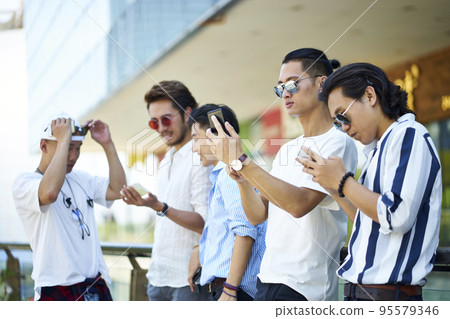 group of five young asian men playing with cellphones outdoors group of five young asian men playing with cellphones outdoors 95579346