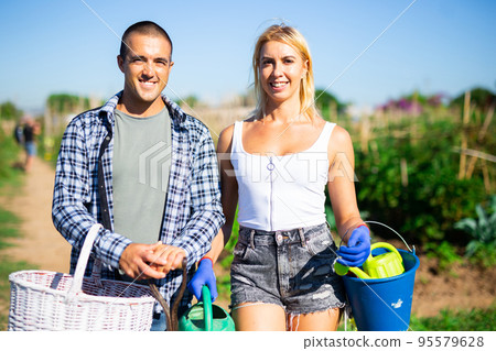 Cheerful couple posing with garden tools outdoors Cheerful couple posing with garden tools outdoors 95579628