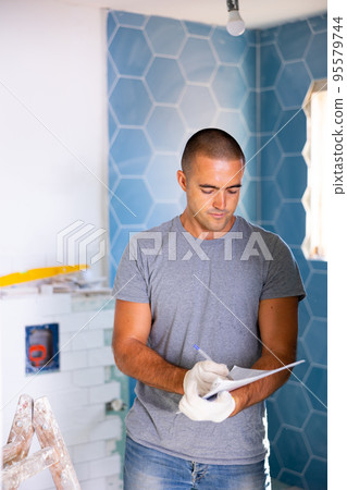 Portrait of young man builder with documents in hands checks quality of completed repairs 95579744