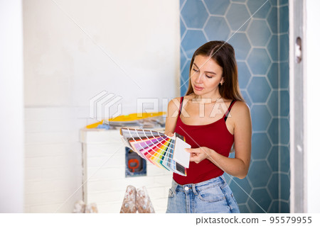 Beautiful young woman choosing tiles color samples in apartment 95579955
