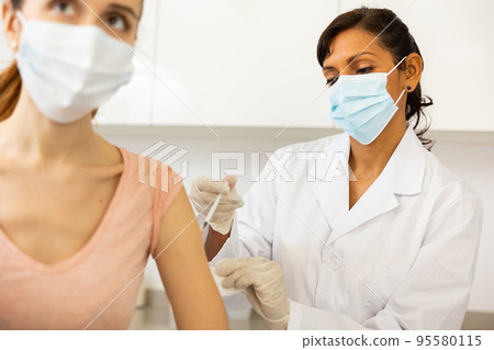 Woman doctor in face mask vaccinating patient Woman doctor in face mask vaccinating patient 95580115