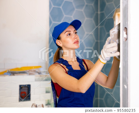 The technology of laying tile, repair and decoration. Focused woman puts porcelain tiles on wall at bathroom The technology of laying tile, repair and decoration. Focused woman puts porcelain tiles on wall at bathroom 95580235
